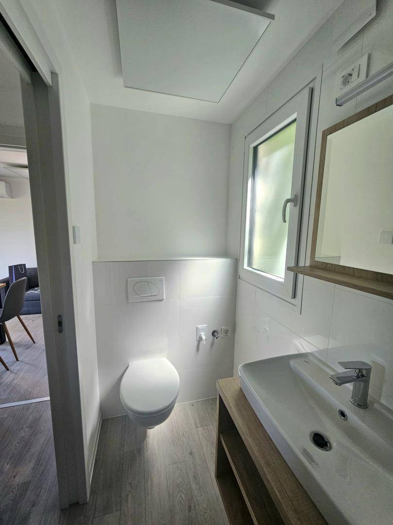 Helles Badezimmer mit wandhängendem WC, Waschtisch und Fenster für Tageslicht.