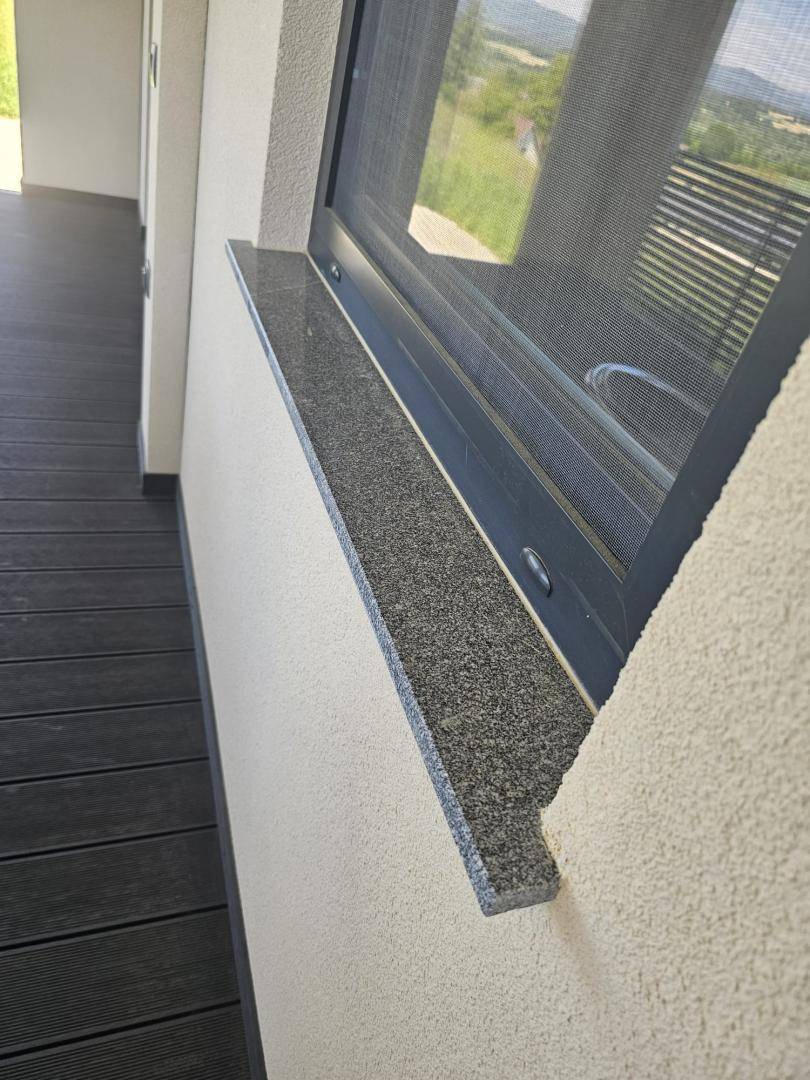 Detailaufnahme eines Fensters mit dunkler Granitfensterbank und Blick ins Grüne.