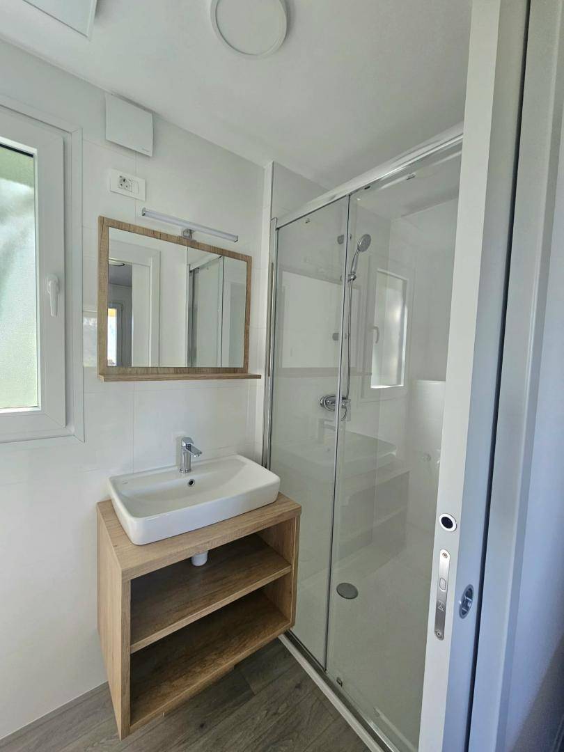 Modernes Badezimmer mit Waschtisch, Spiegel und Duschkabine, hell gefliest.