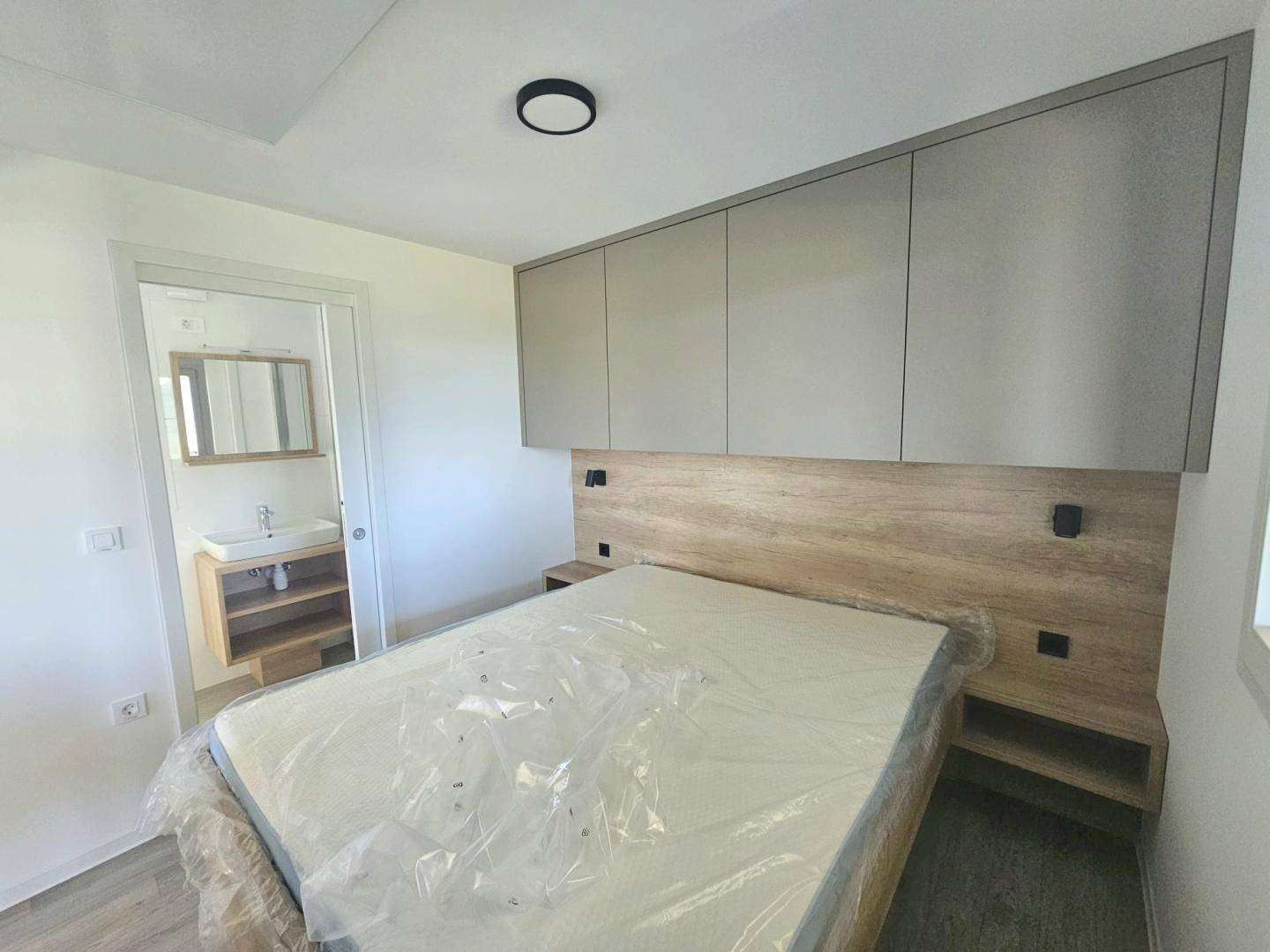 Helles Schlafzimmer mit Bett und direktem Zugang zum modernen Badezimmer.