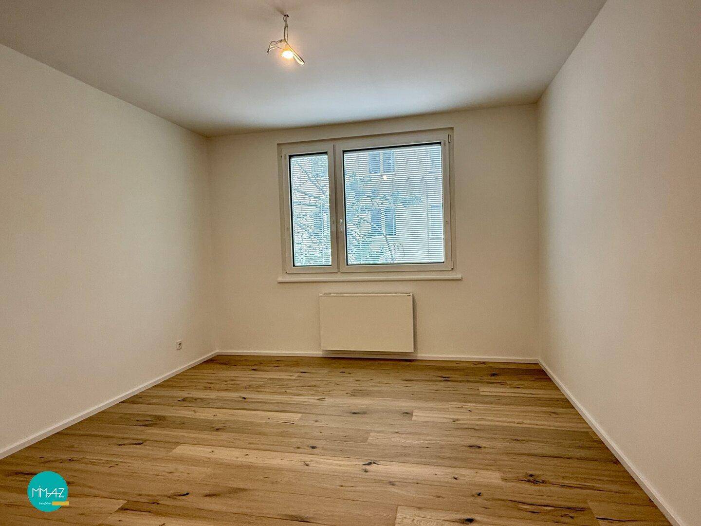 Helles Schlafzimmer mit Parkettboden und großem Fenster, bereit zur individuellen Gestaltung.