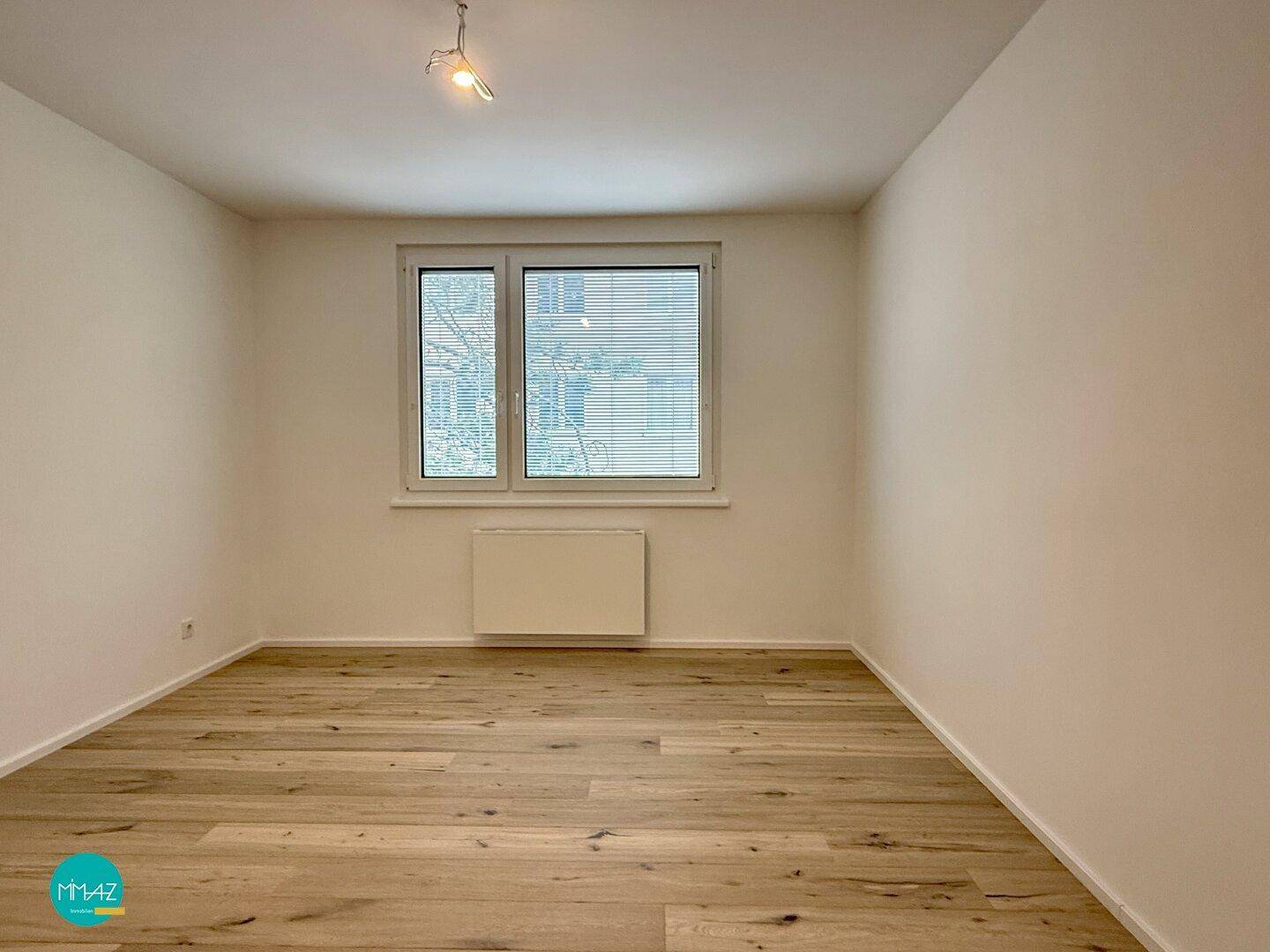 Helles Schlafzimmer mit Parkettboden und großem Fenster, bereit zur individuellen Gestaltung.
