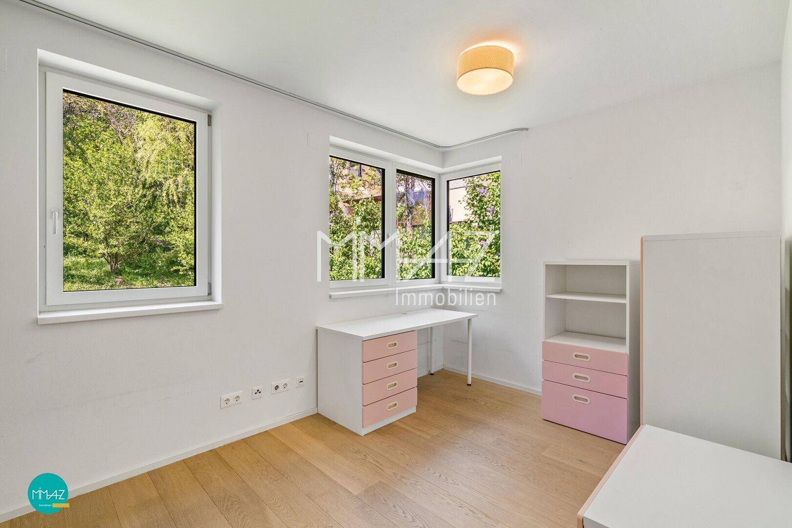Helles Schlafzimmer oder Kinderzimmer mit Holzboden, großen Fenstern und Blick ins Grüne.