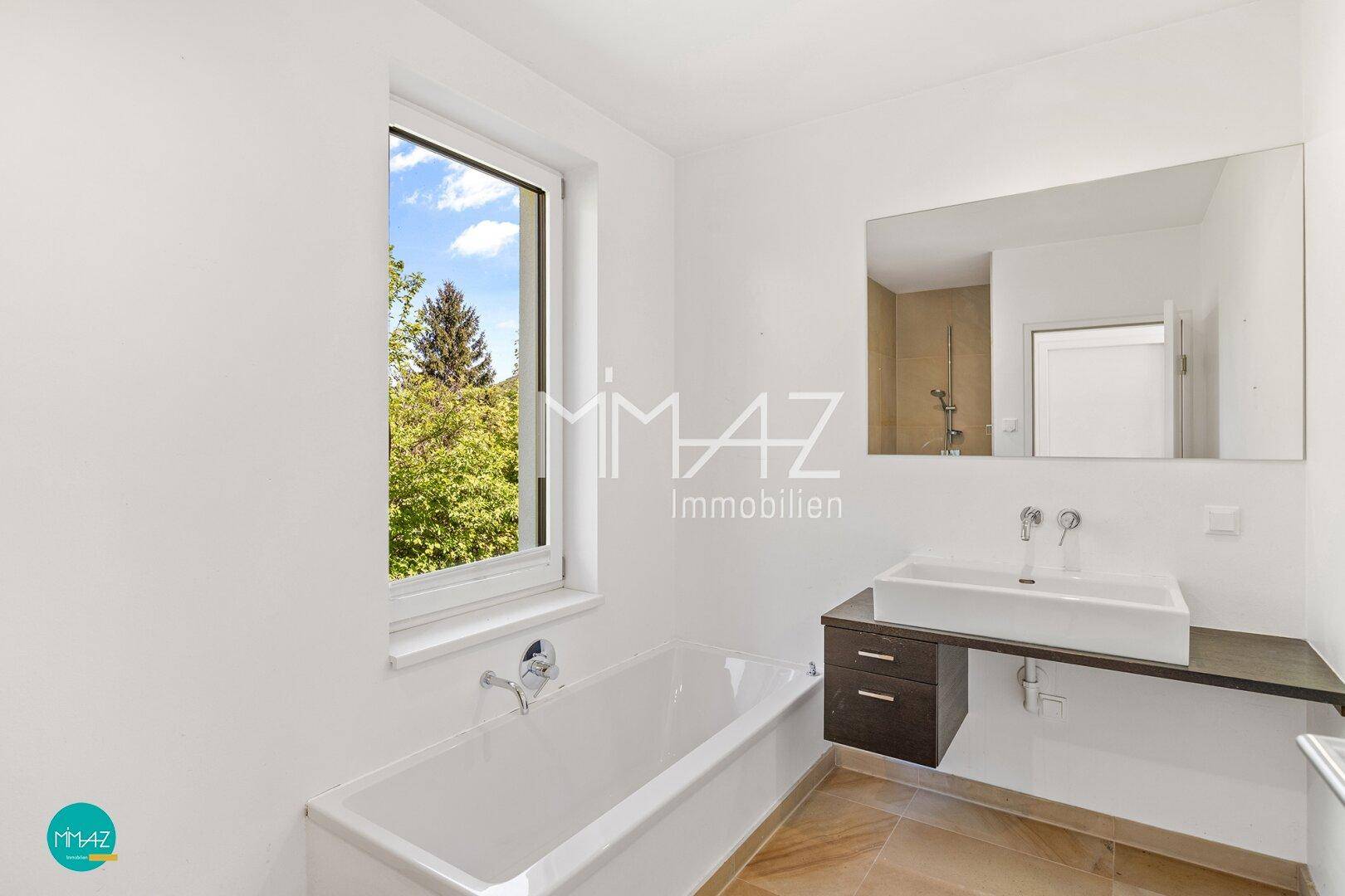 Modernes Badezimmer mit Badewanne, Einzelwaschbecken und Fenster mit Blick ins Grüne.
