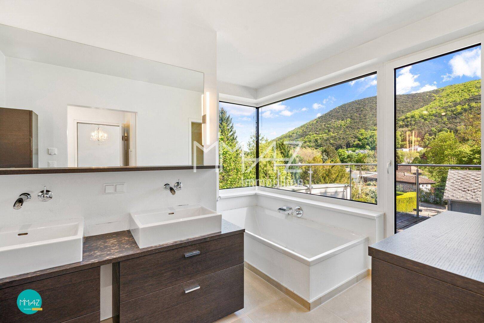 Luxuriöses Badezimmer mit Doppelwaschbecken, Badewanne und Panoramafenstern mit Bergblick.