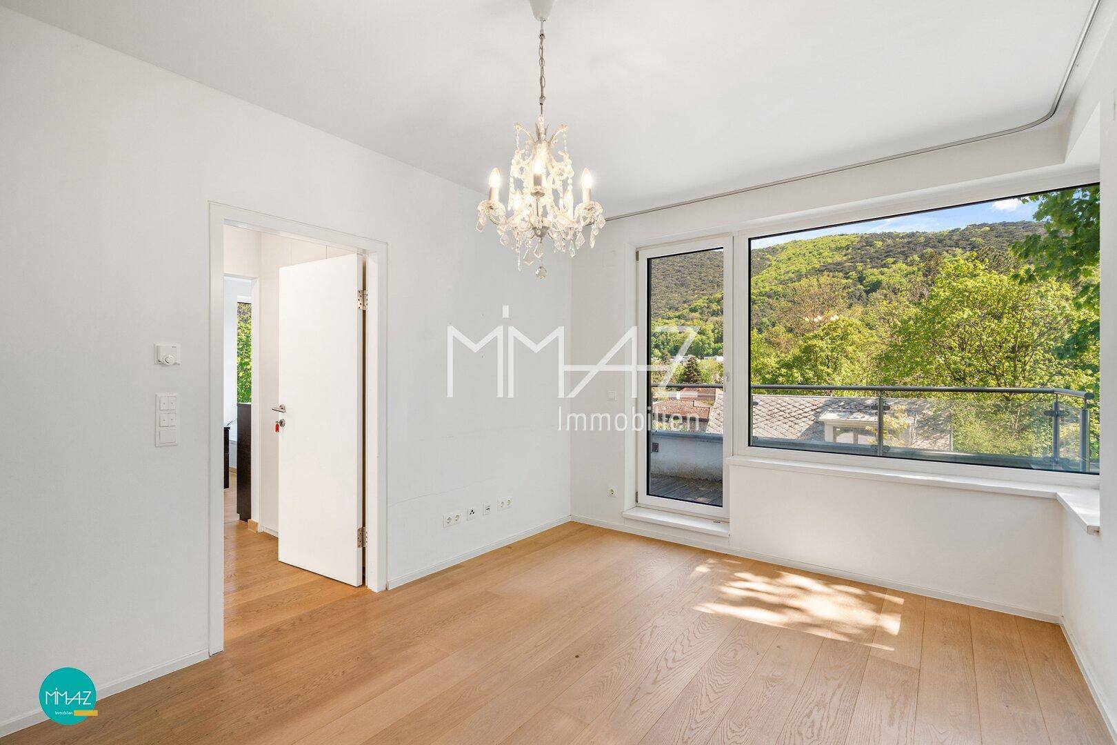 Helles Schlafzimmer mit Holzboden, Kronleuchter und Zugang zu einem Balkon mit Bergblick.
