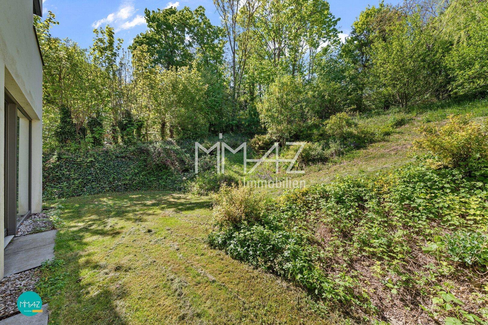 Naturbelassener Gartenbereich mit Rasen und üppiger Vegetation an einem Hang.