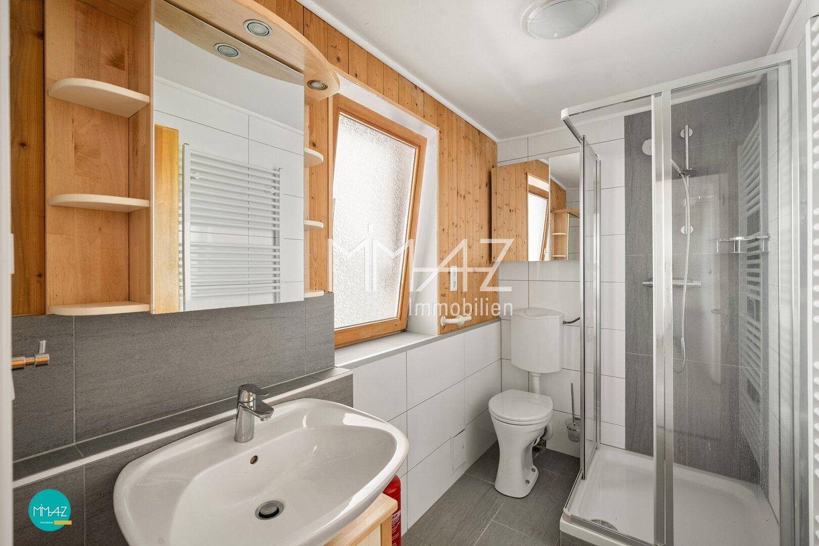 Helles Badezimmer mit Dusche, WC, Waschbecken und Holzverkleidung an den Wänden.
