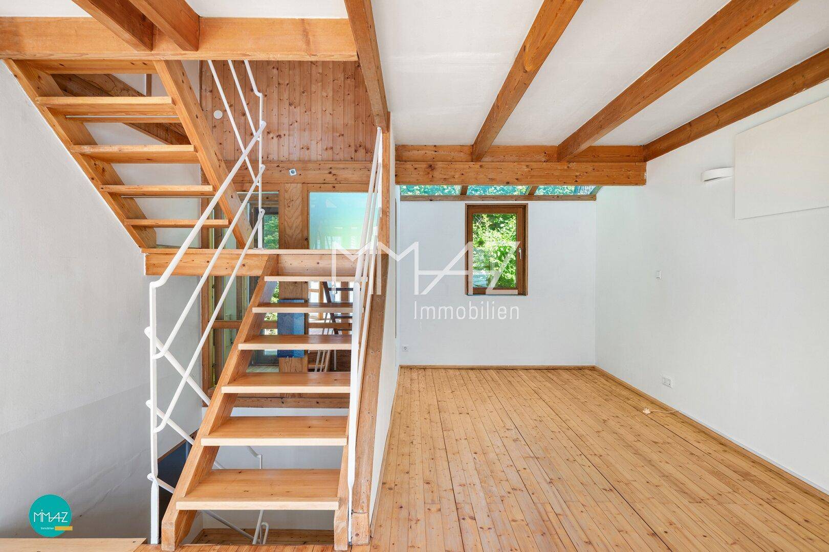 Heller Wohnbereich mit Holztreppe, Dielenboden und einem Fenster mit Blick ins Grüne.