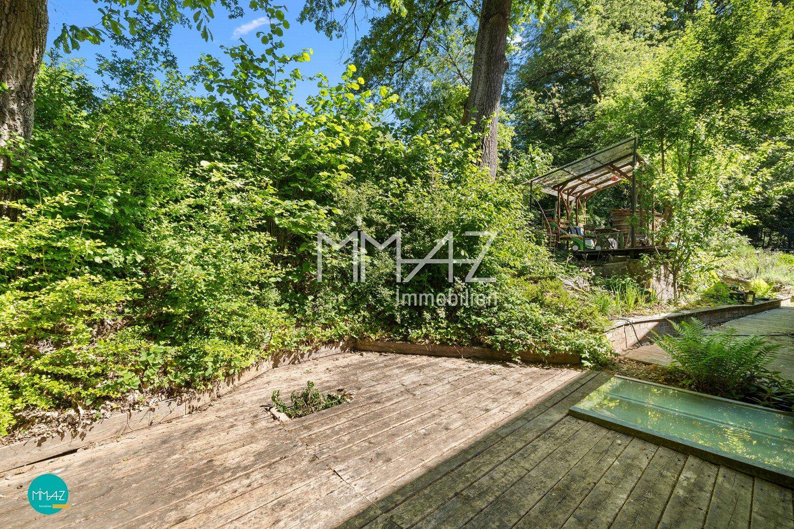 Naturnaher Gartenbereich mit Holzterrasse, üppiger Vegetation und einem kleinen Gartenhaus.