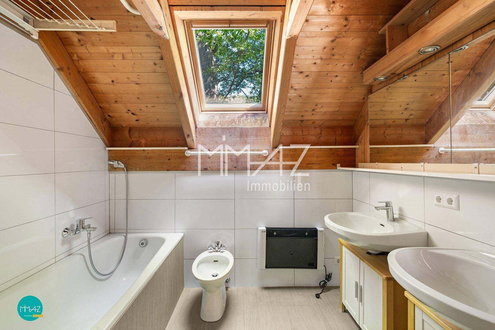 Dachbad mit Badewanne, Bidet, Doppelwaschbecken und Dachfenster für natürliches Licht.