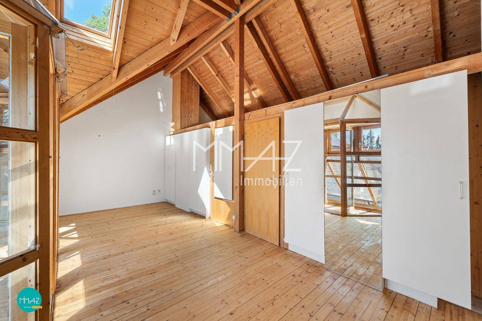 Geräumiges Dachzimmer mit sichtbaren Holzbalken, Dielenboden und Dachfenstern für viel Licht.
