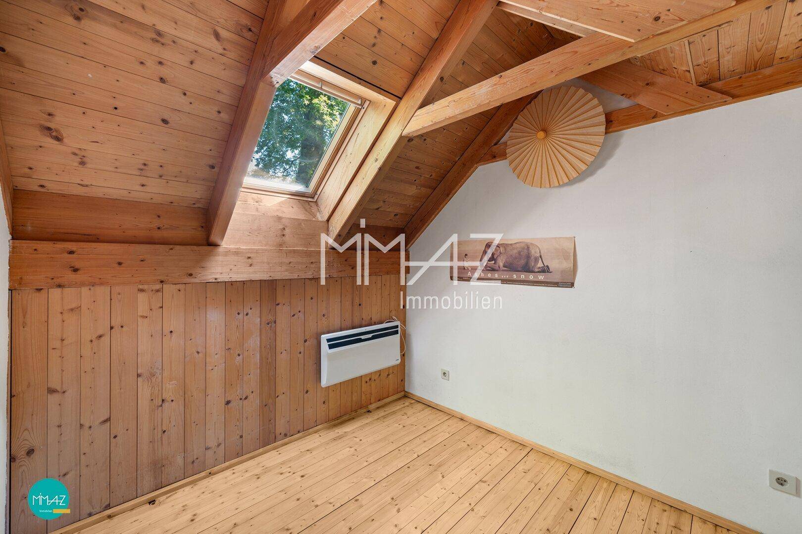 Gemütliches Dachzimmer mit Holzverkleidung, Dielenboden und Dachfenster.