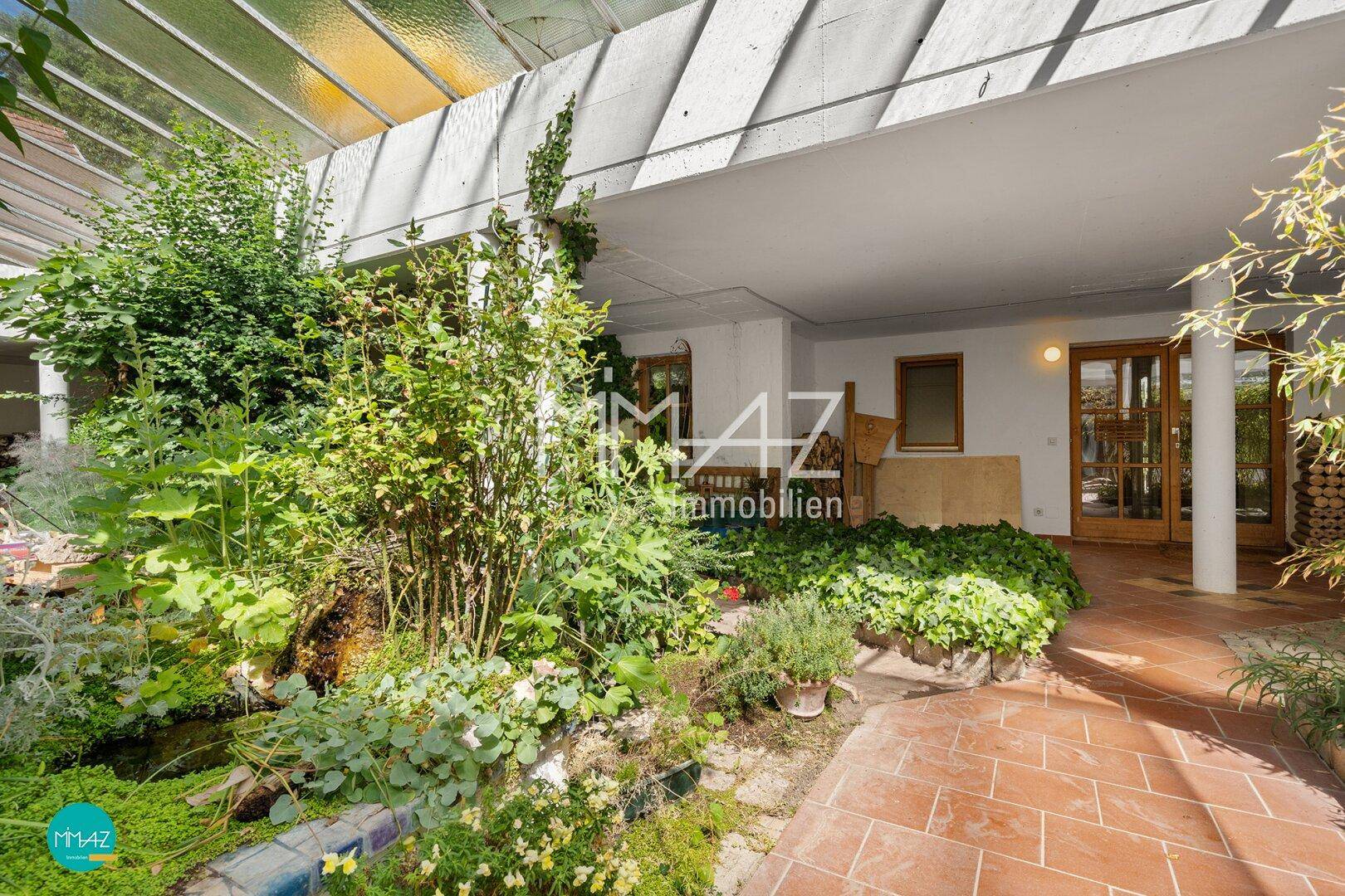 Mediterraner Gartenbereich mit üppiger Bepflanzung, Teich und überdachtem Terrassenbereich.