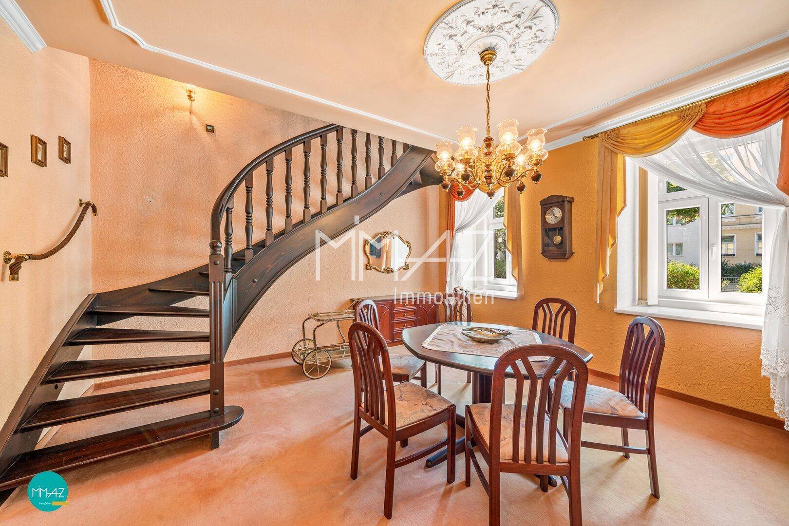 Eleganter Essbereich mit einer geschwungenen Holztreppe, Kronleuchter und Blick nach draußen.