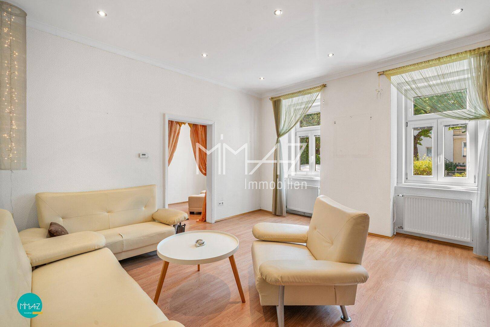 Helles Wohnzimmer mit Parkettboden, beigen Sofas und großen Fenstern mit Blick ins Grüne.