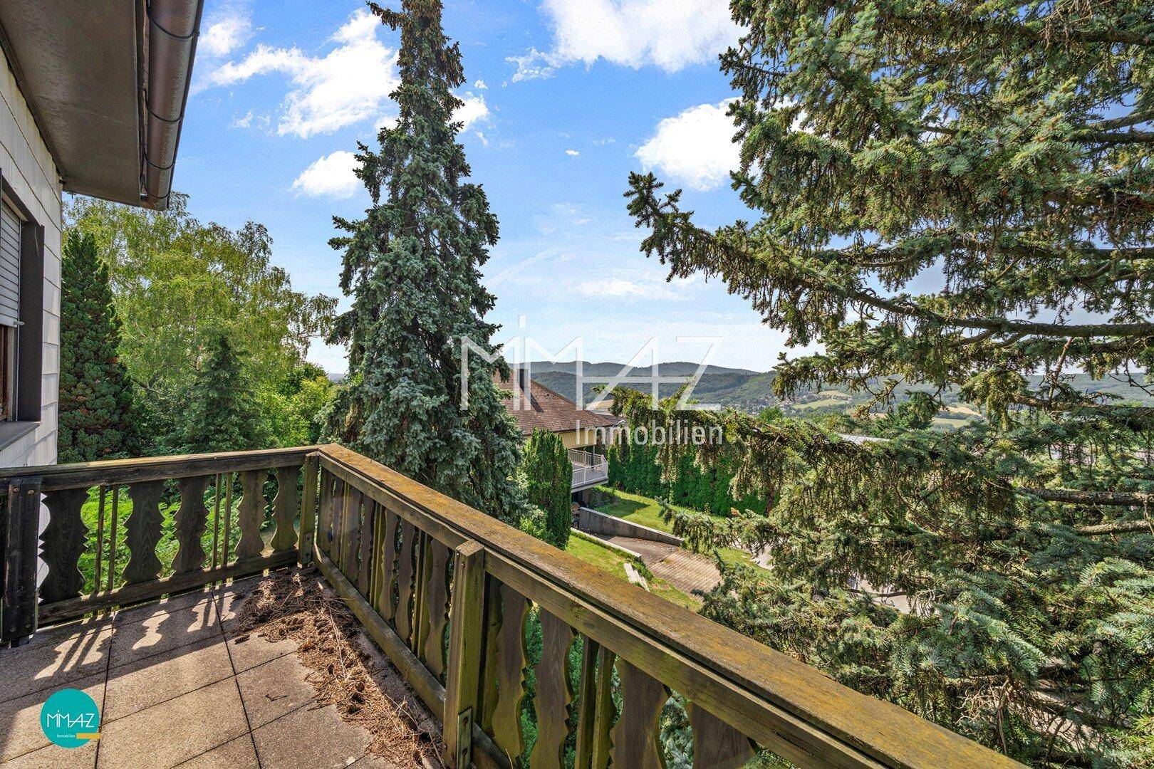 Rustikaler Holzbalkon mit Blick auf die grüne Hügellandschaft und weitere Häuser.