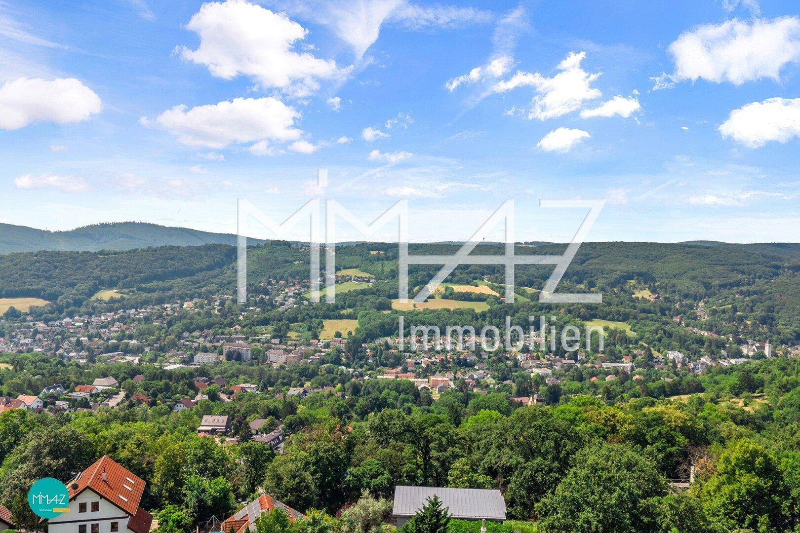 Weitläufiger Panoramablick über eine grüne Hügellandschaft mit Siedlungen und blauem Himmel.