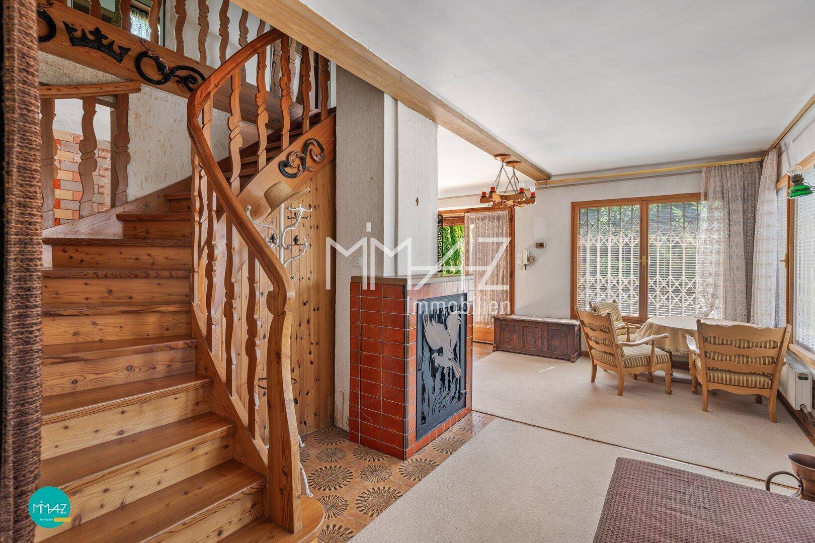 Rustikaler Eingangsbereich mit Holztreppe, Kachelofen und Zugang zum Wohnbereich.