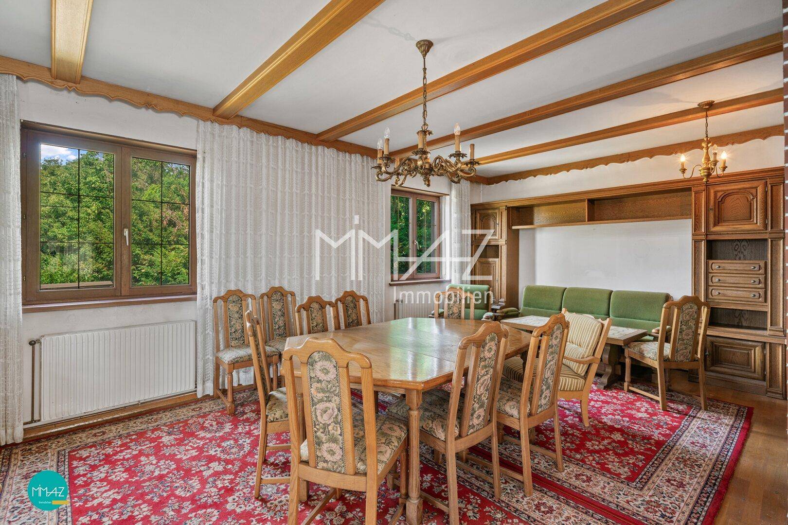 Gemütlicher Essbereich mit großem Holztisch, passenden Stühlen und sichtbaren Deckenbalken.