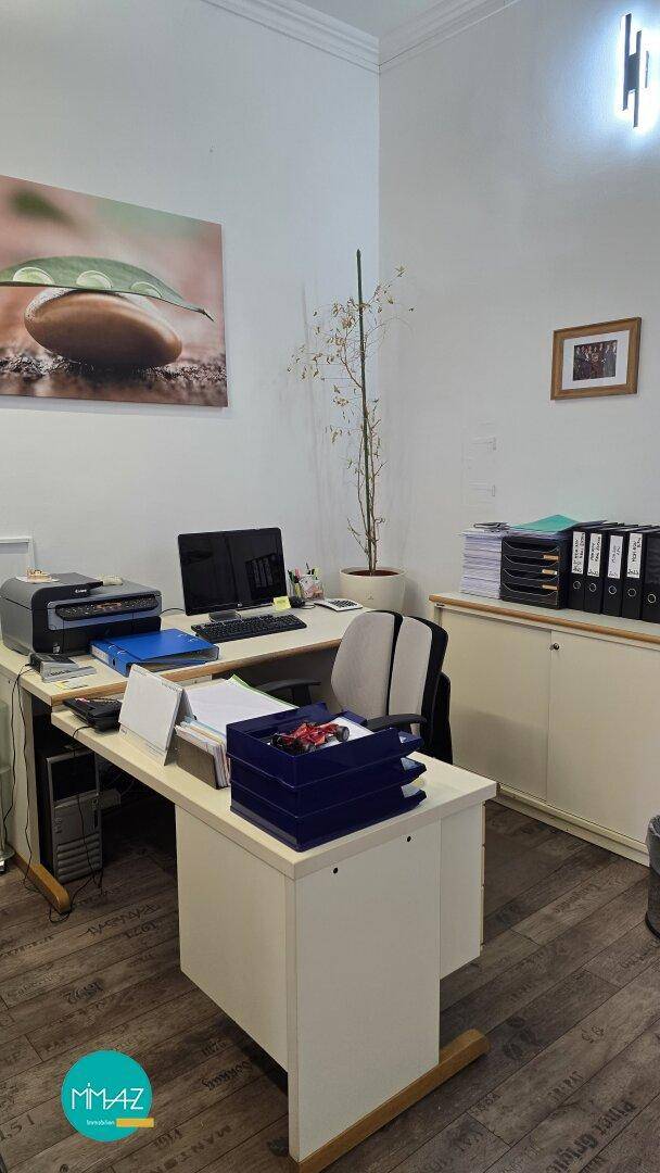 Arbeitsplatz in einem Büro mit Schreibtisch, Computer und Drucker, umgeben von hellen Wänden.