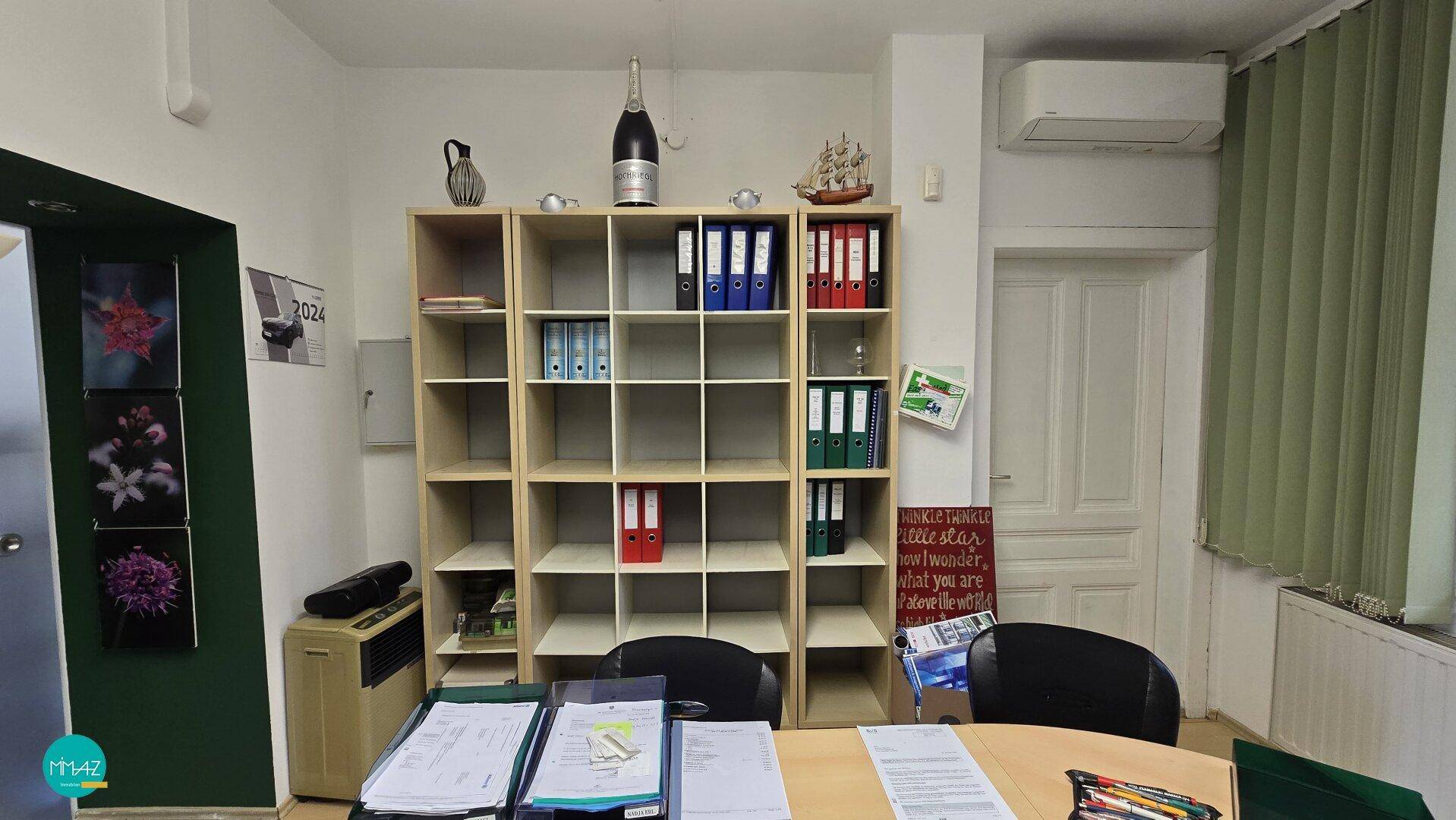 Büro mit Regalsystem, Aktenordnern und einer Klimaanlage über der Tür, ordentlich und funktional.