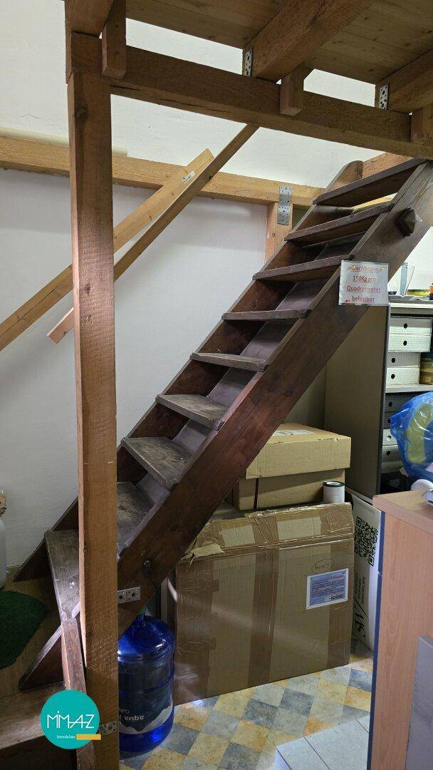 Holztreppe führt zu einer oberen Ebene, mit sichtbaren Holzbalken und Lagerbereich darunter.