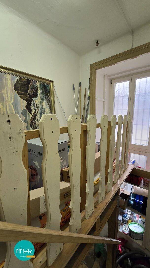 Treppenaufgang mit Holzgeländer und Fenster im Hintergrund, führt zu einer oberen Etage.