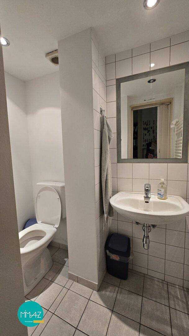 Einfache Toilette mit Waschbecken und Spiegel, gefliest und funktional ausgestattet.