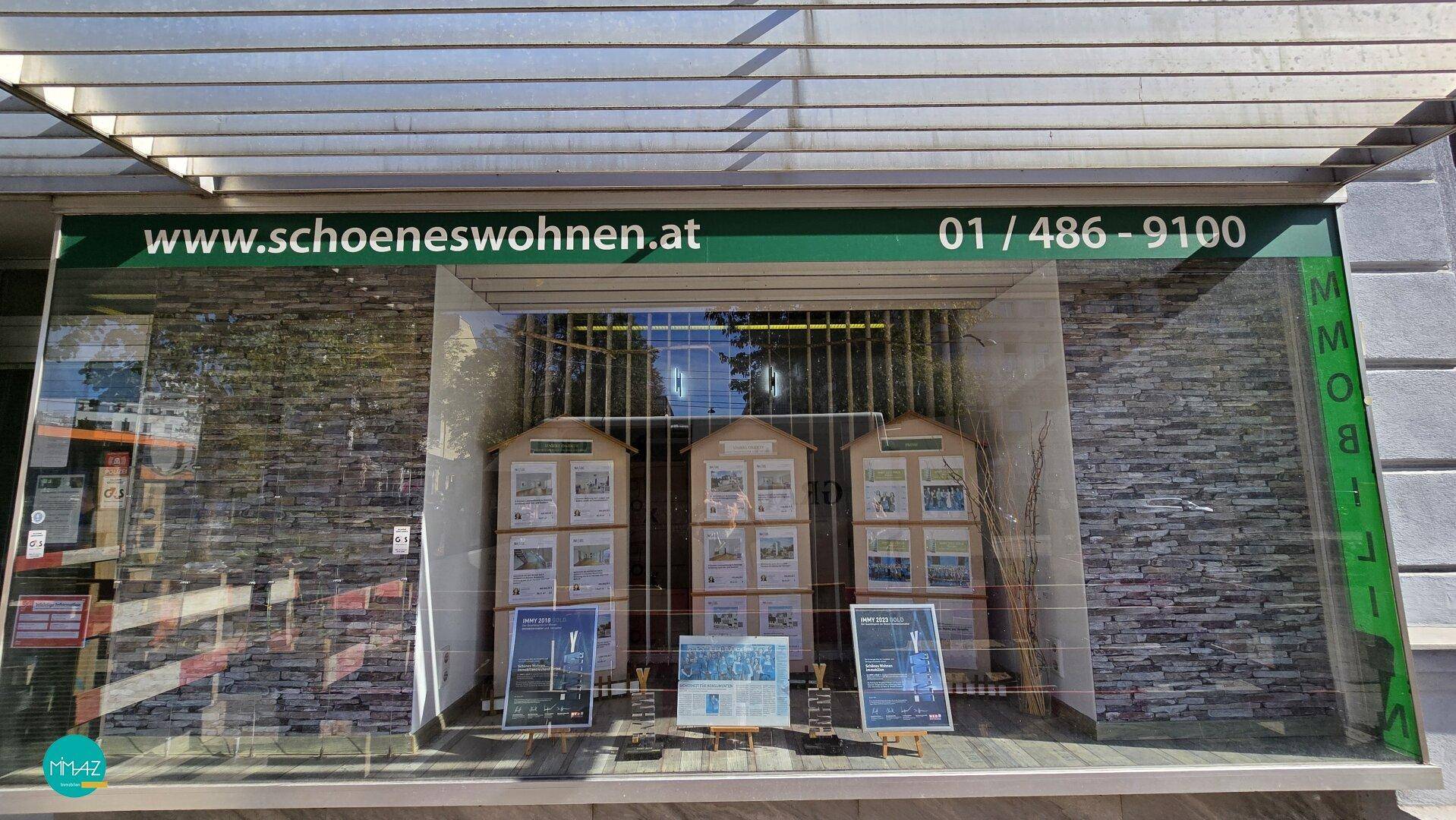 Schaufenster eines Geschäfts mit Immobilienanzeigen und Firmenlogo, einladend gestaltet.
