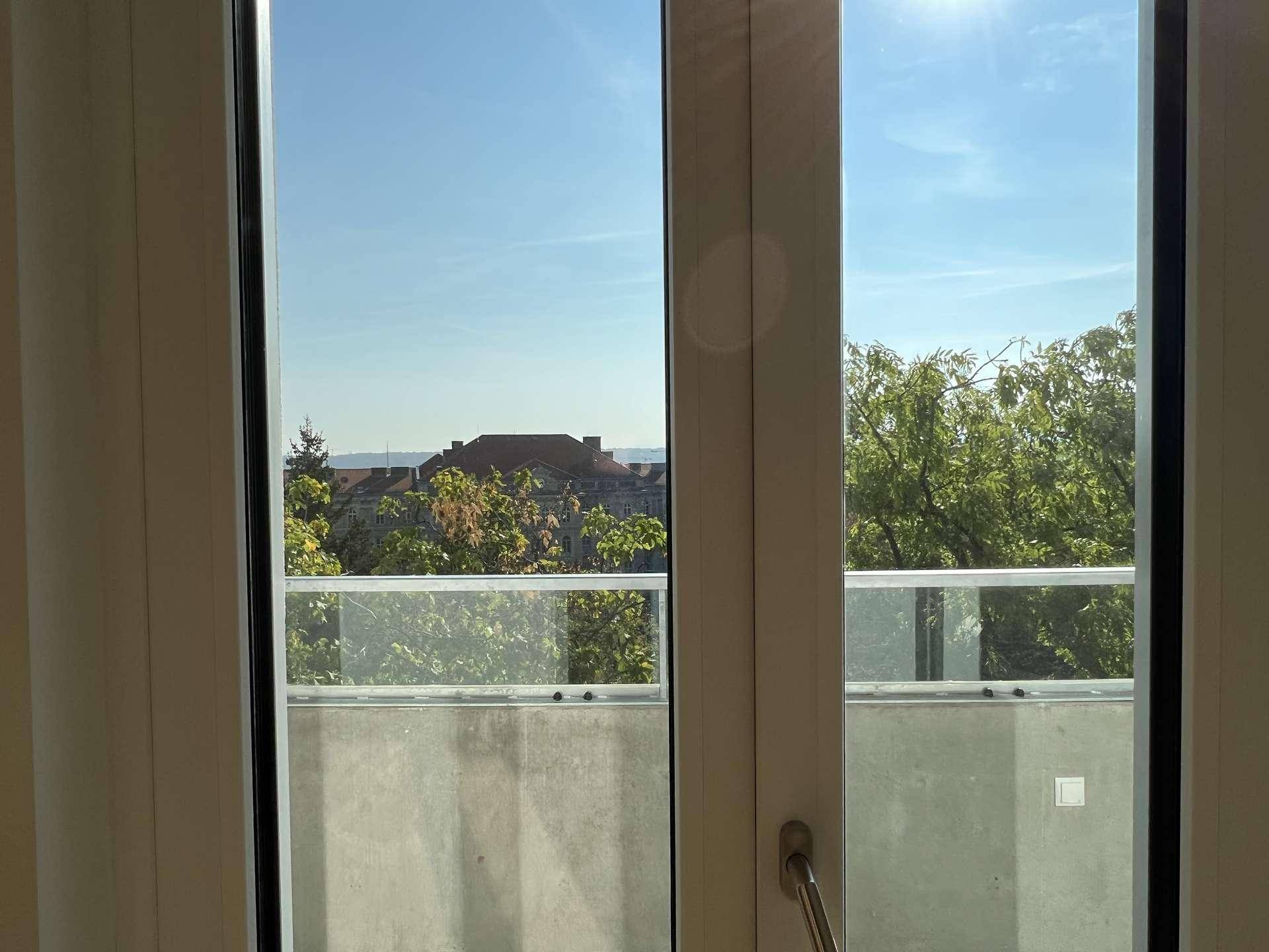Weitblick vom Balkon über die Stadt und grüne Baumwipfel.