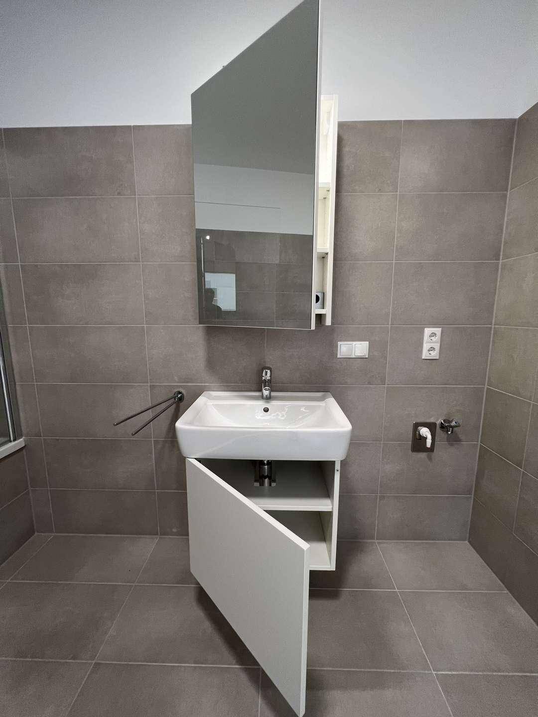 Moderner Waschtisch mit Unterschrank und Spiegelkabinett in einem gefliesten Bad.
