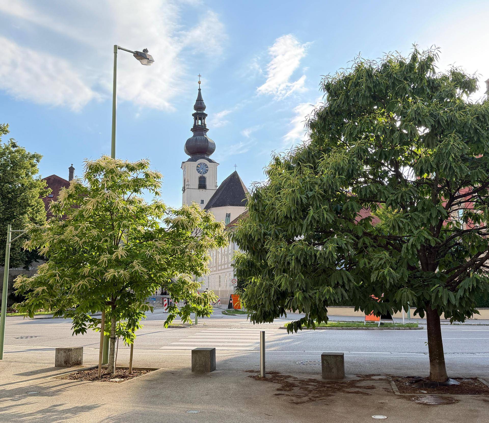 Blick auf eine historische Kirche mit Zwiebelturm und umliegende Bäume an einem sonnigen Tag.