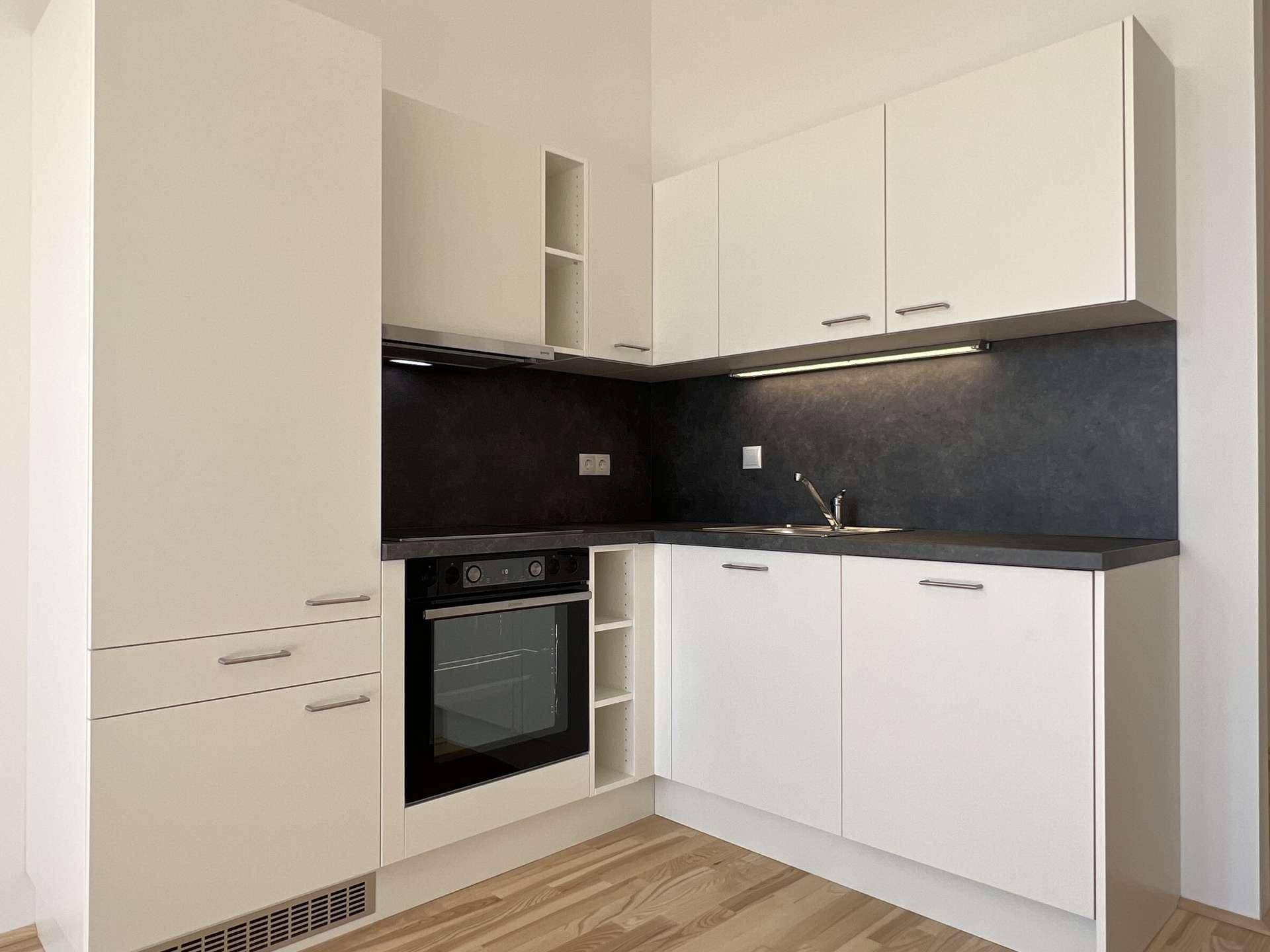 Moderne Einbauküche mit weißen Fronten, dunkler Arbeitsplatte und integriertem Backofen.