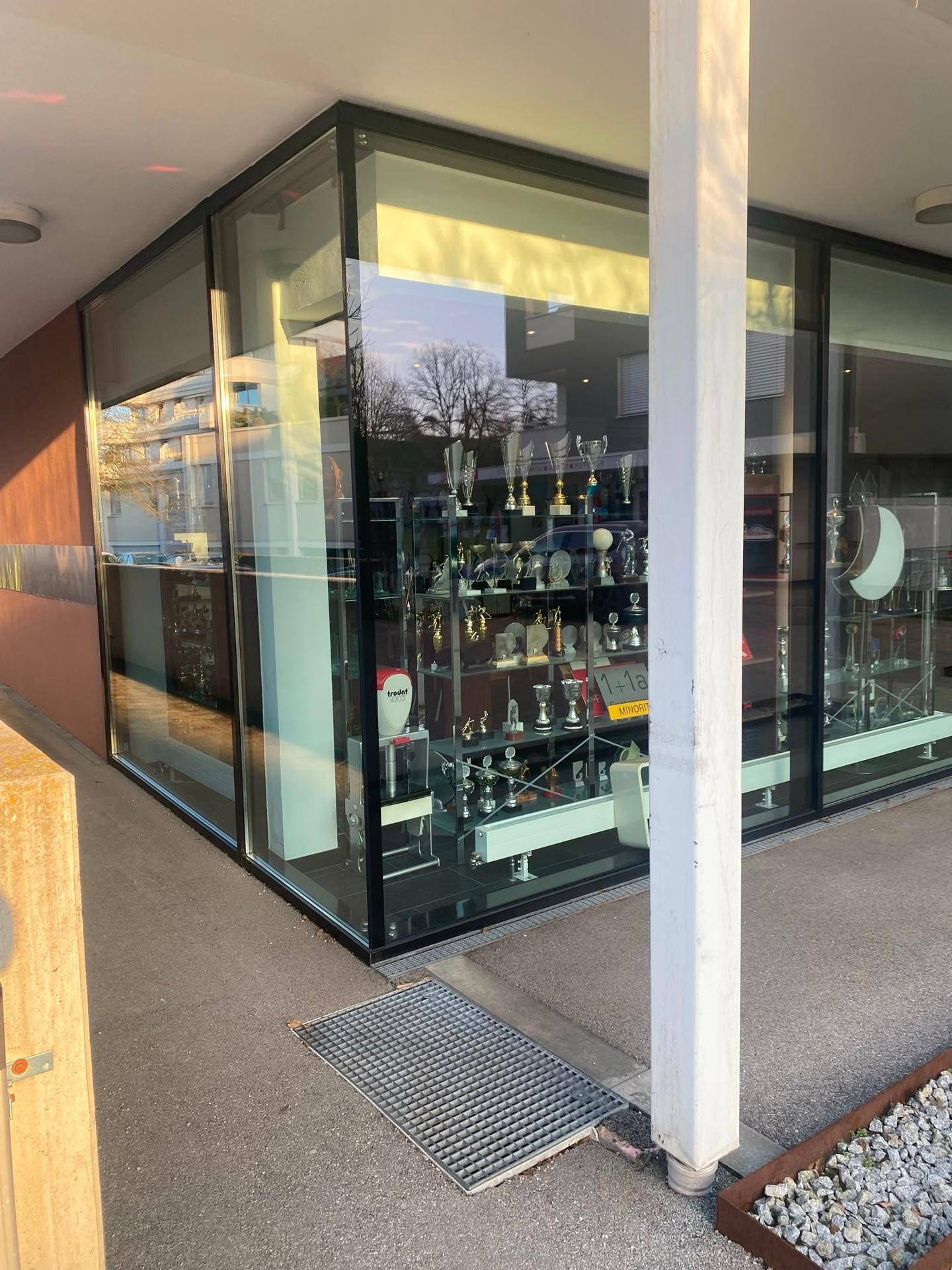 Nahaufnahme der Ecke eines Geschäftsgebäudes mit großen Glasfenstern, die Pokale ausstellen.