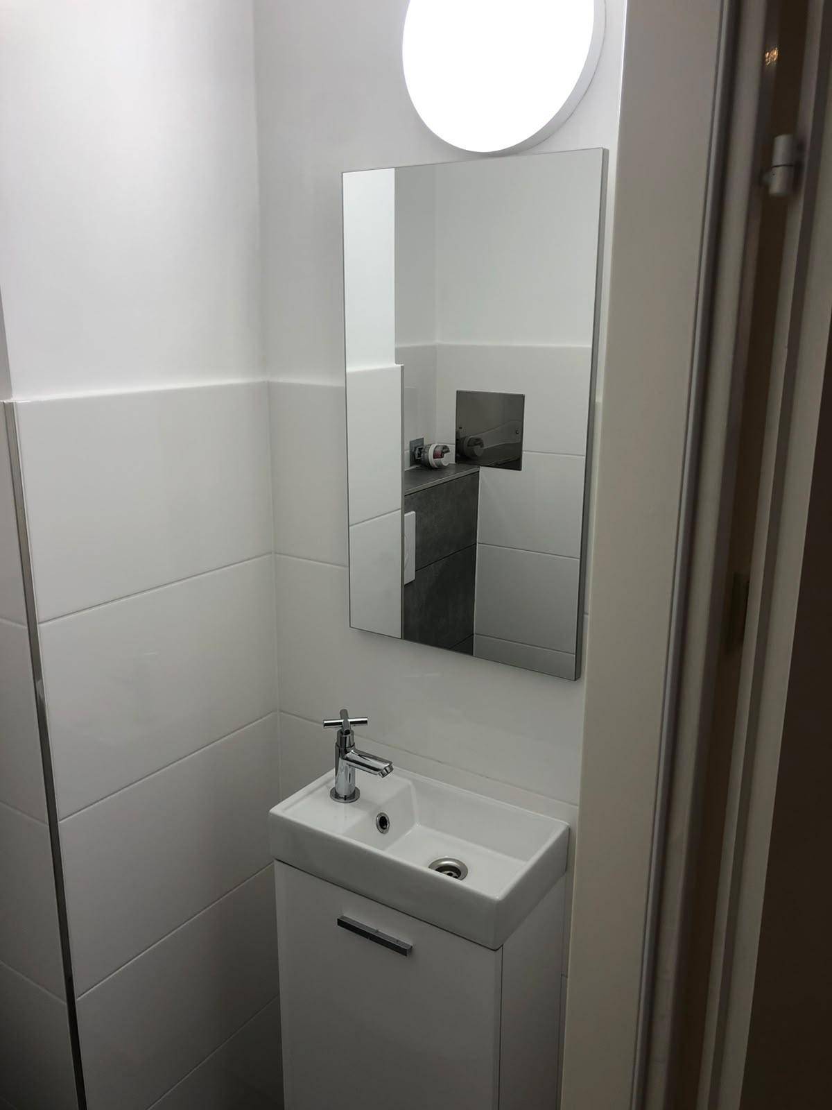 Kleines Gäste-WC mit modernem Waschtisch und Spiegel, hell gefliest.