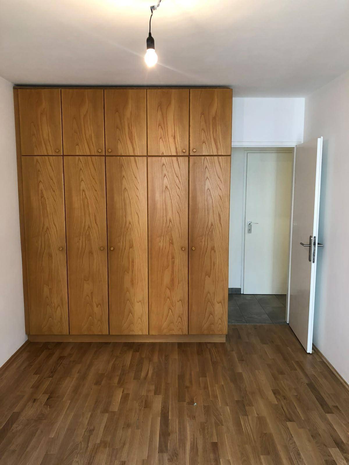 Schlafzimmer mit hellem Parkettboden und großem, integriertem Holzschrank.