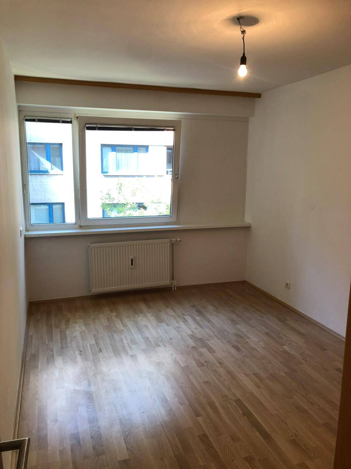 Helles Schlafzimmer mit Parkettboden, Fenster und Heizkörper unter der Fensterbank.