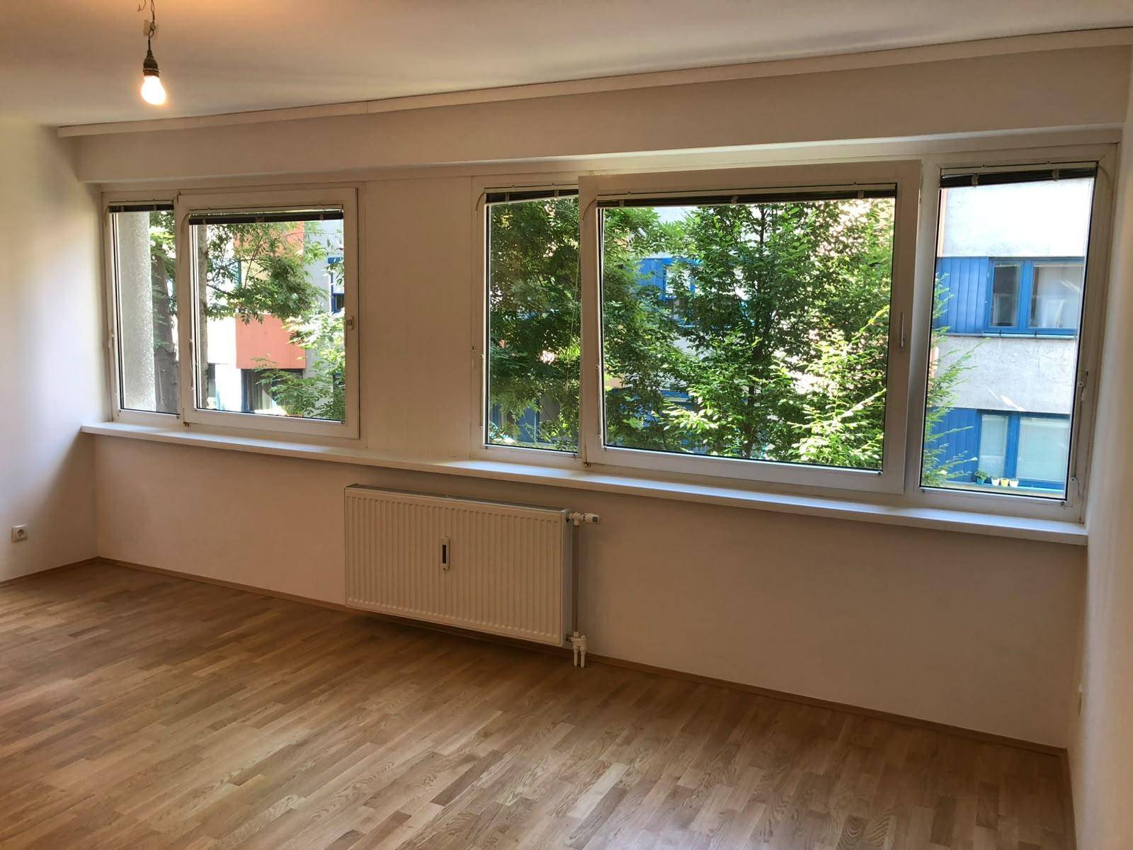 Helle Fensterfront im Wohnzimmer mit Blick ins Grüne und Heizkörper unter den Fenstern.