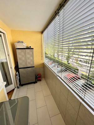 Überdachter Balkon mit Fliesenboden, Jalousien und Blick auf die Straße.