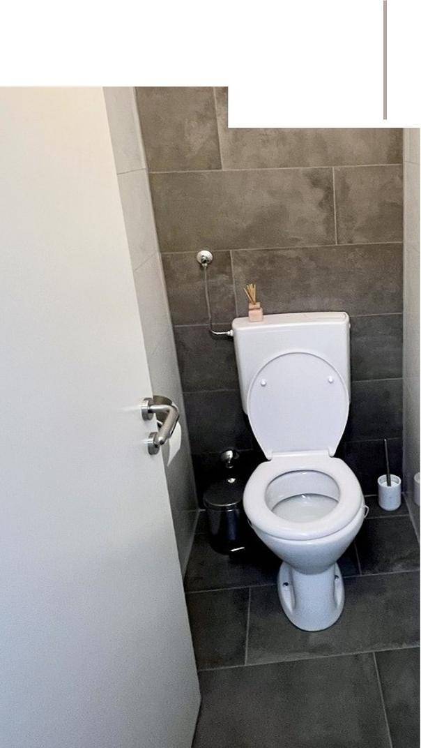 Separates WC mit dunklen Fliesen und moderner Toilette.