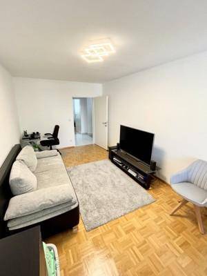 Helles Wohnzimmer mit Sofa, Fernseher und Arbeitsbereich.