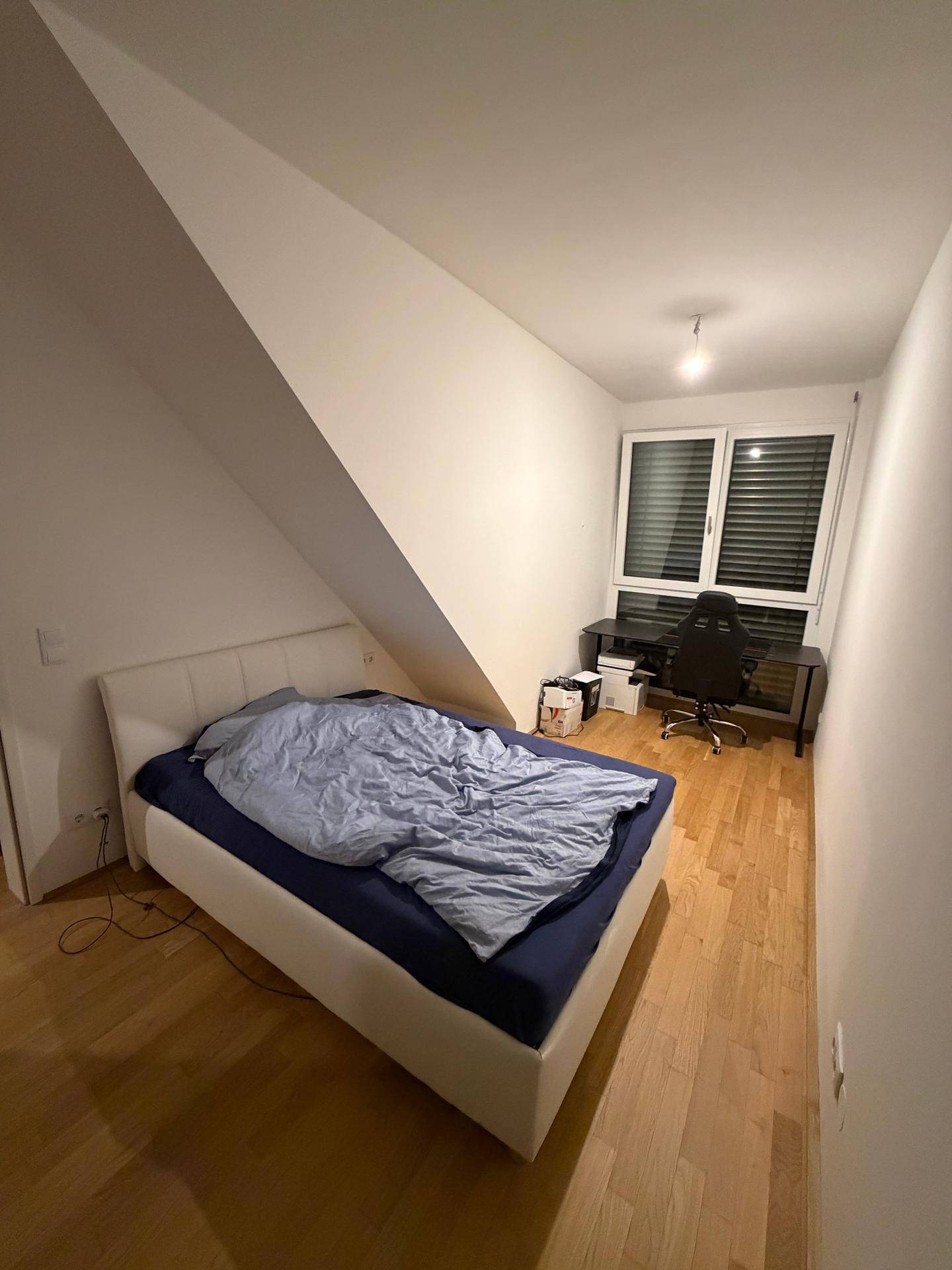 Schlafzimmer mit Doppelbett, Schreibtisch und Dachschräge, ausgestattet mit Holzboden.