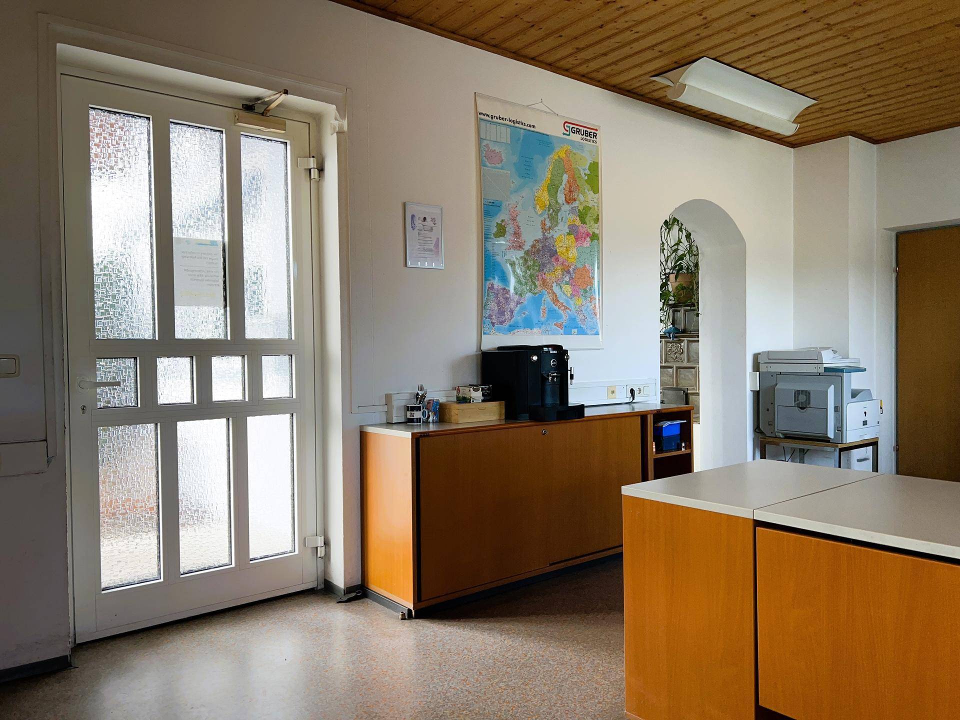 Eingangsbereich des Büros mit Glastür und einem Sideboard, das als Empfangsbereich dienen könnte.