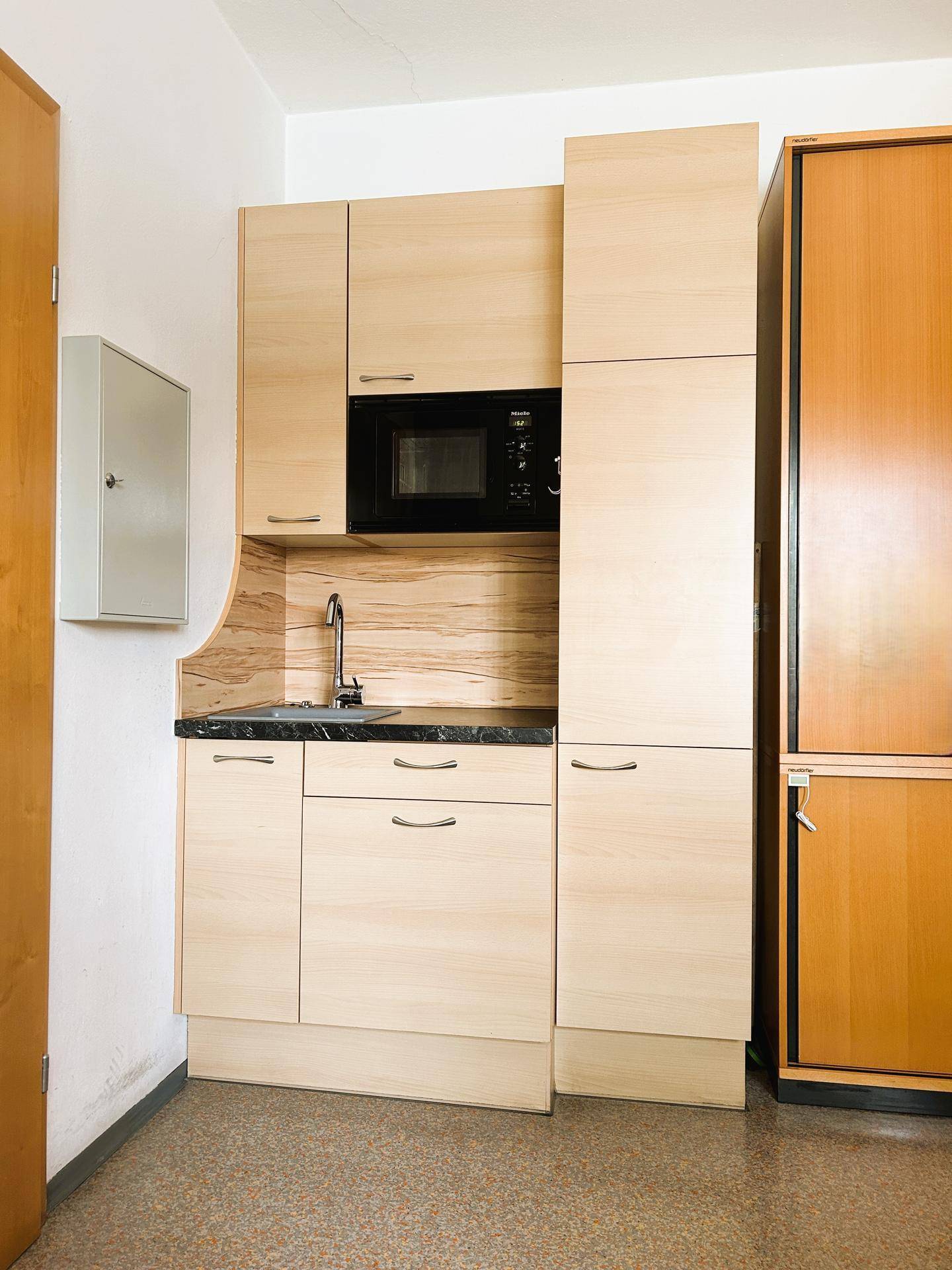 Kompakte Küchenzeile mit Spüle, Mikrowelle und hellen Holzschränken, ideal für kleine Büros.