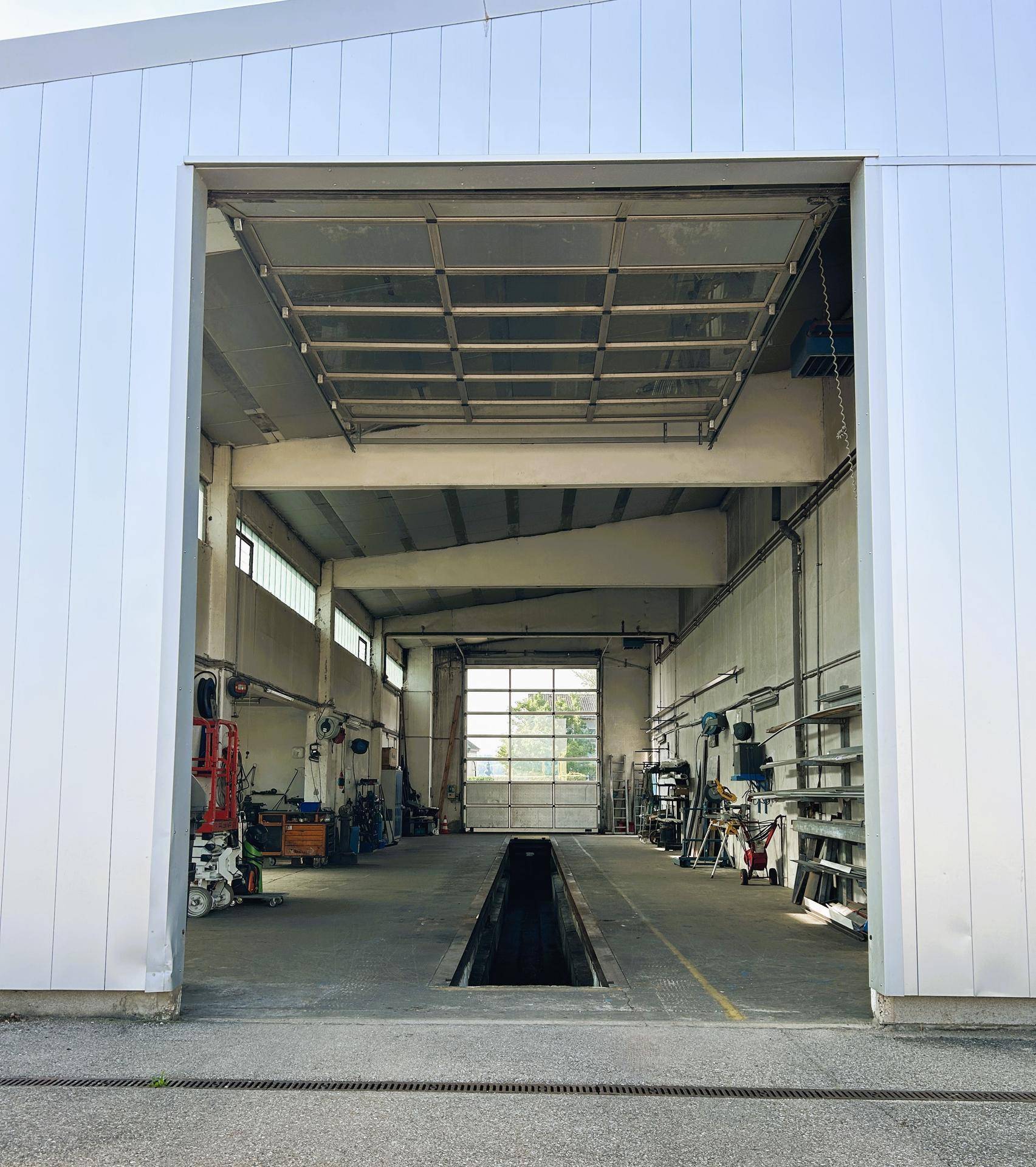 Eingangsbereich der Werkstatthalle mit offenem Rolltor und Blick auf die Inspektionsgrube im Inneren.