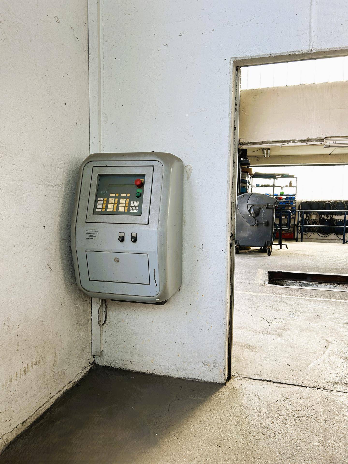 Steuerpult an der Wand, das zur Bedienung der Werkstattanlagen dient, mit Blick in den Arbeitsbereich.