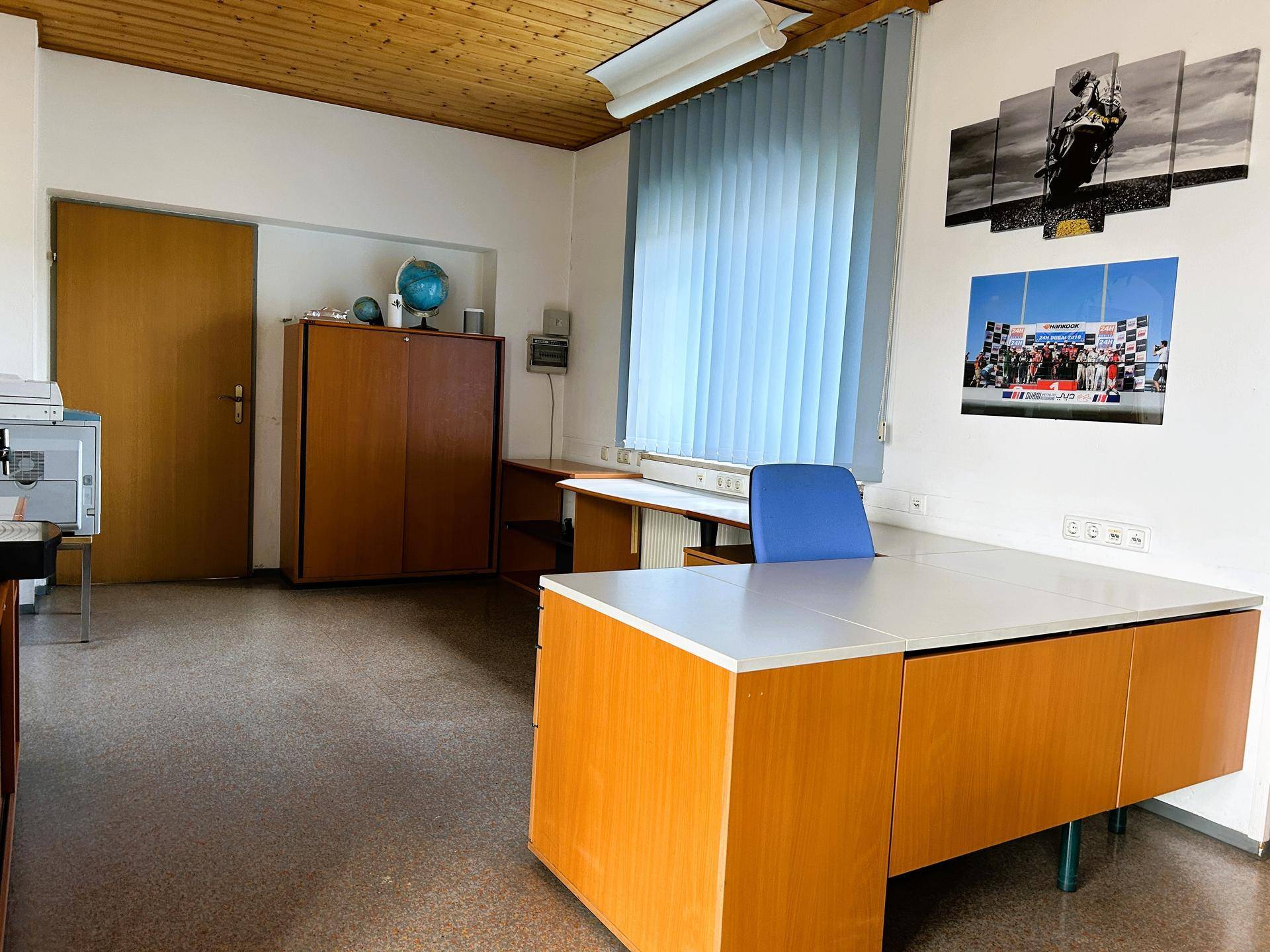 Büro mit Holzdecke und großem Fenster mit Jalousien, ausgestattet mit einem Schreibtisch und Bürostuhl.