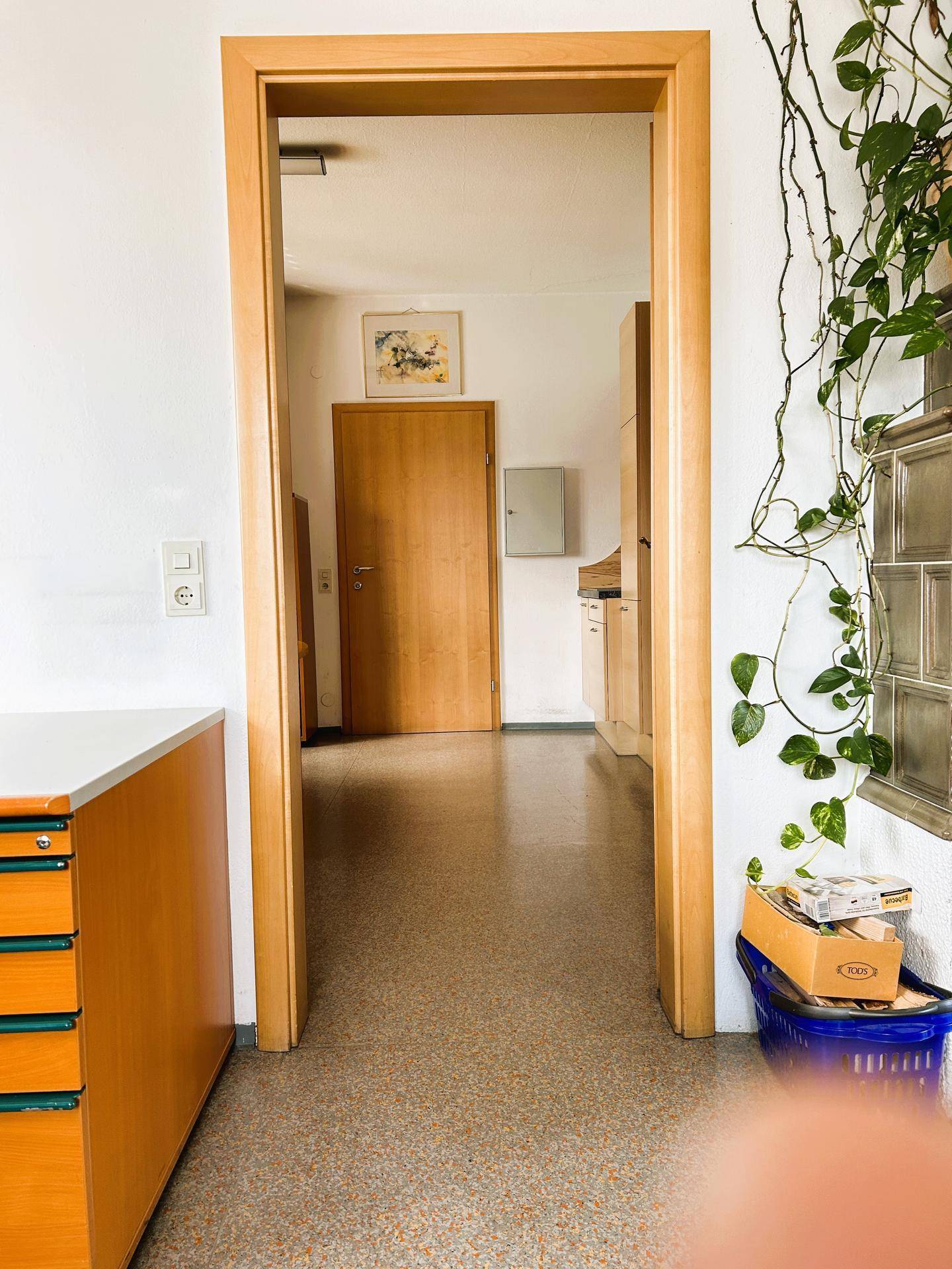 Flur im Bürogebäude mit Holztüren und einem Kachelofen im Hintergrund, der eine gemütliche Atmosphäre schafft.