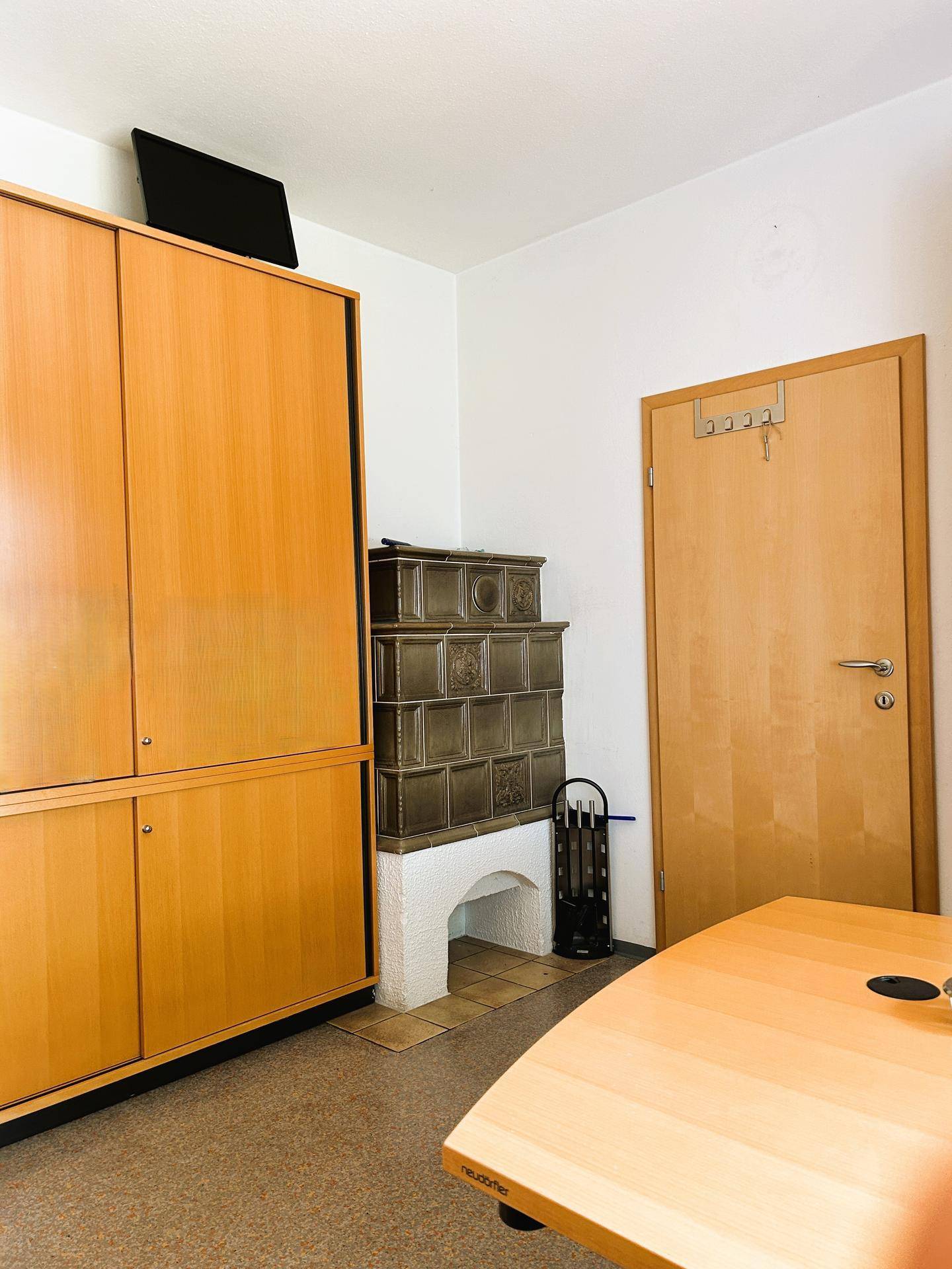 Büro mit einem traditionellen Kachelofen und einem großen Holzschrank, der eine warme Atmosphäre schafft.